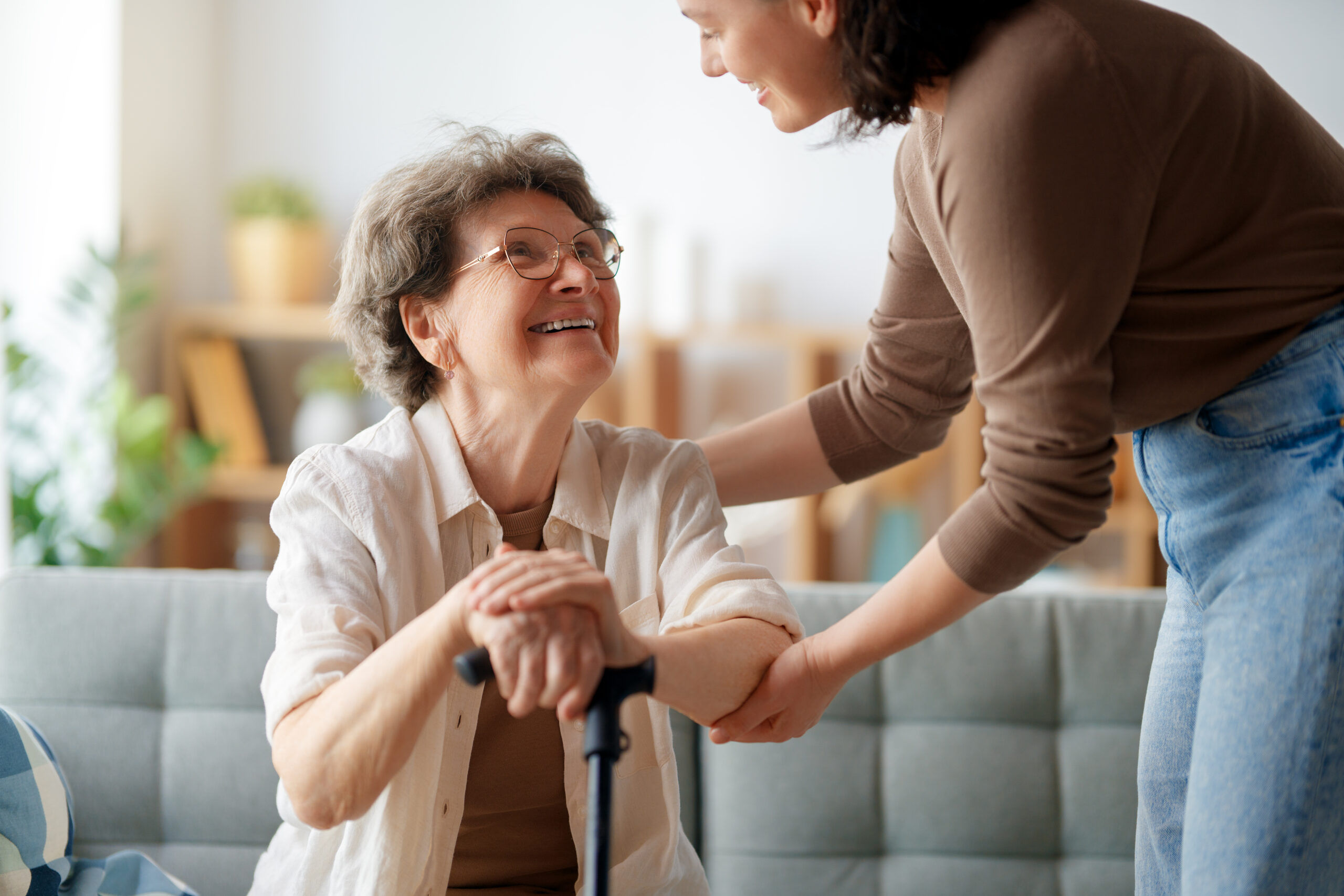 Caregiver assisting elderly woman with mobility support at home, smiling and holding her arm
