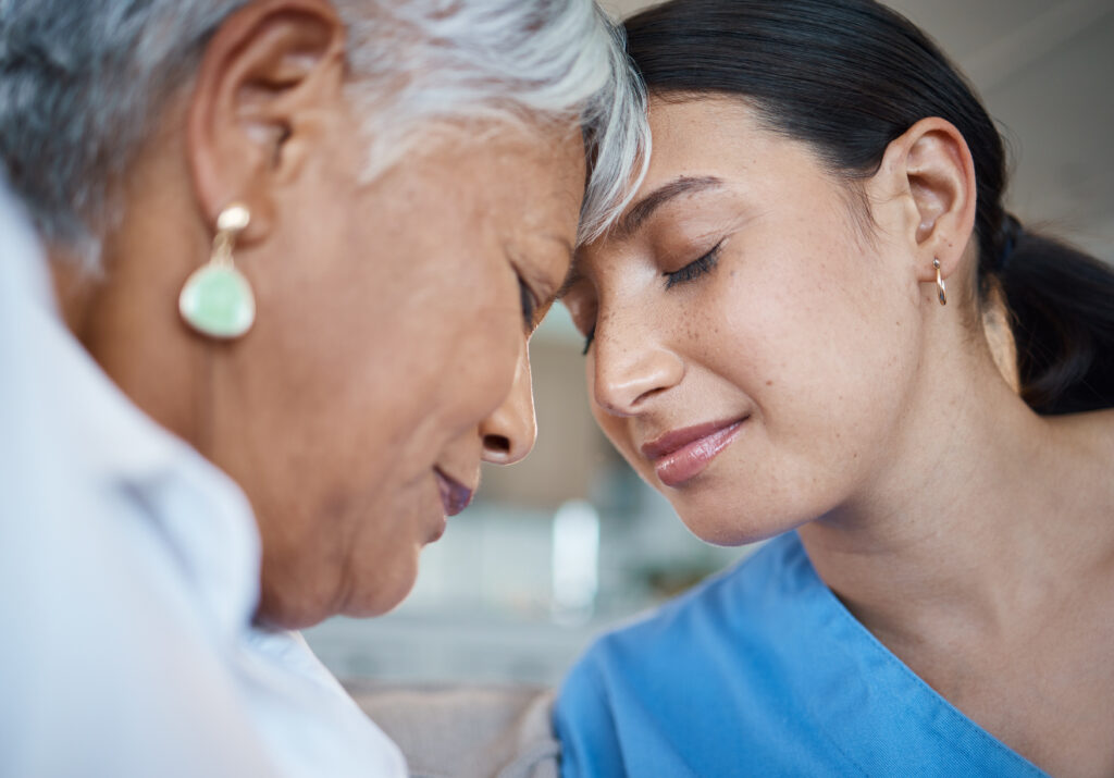 Compassionate nurse comforting elderly patient with gentle forehead touch in healthcare setting