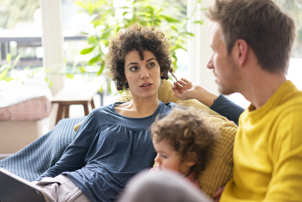 Parents having a thoughtful conversation at home while their child sits nearby, reflecting a family decision-making moment