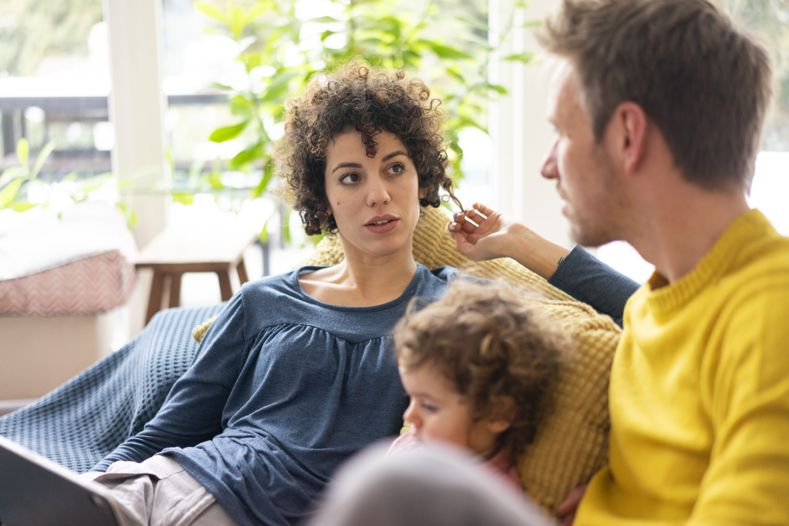 Parents having a thoughtful conversation at home while their child sits nearby, reflecting a family decision-making moment